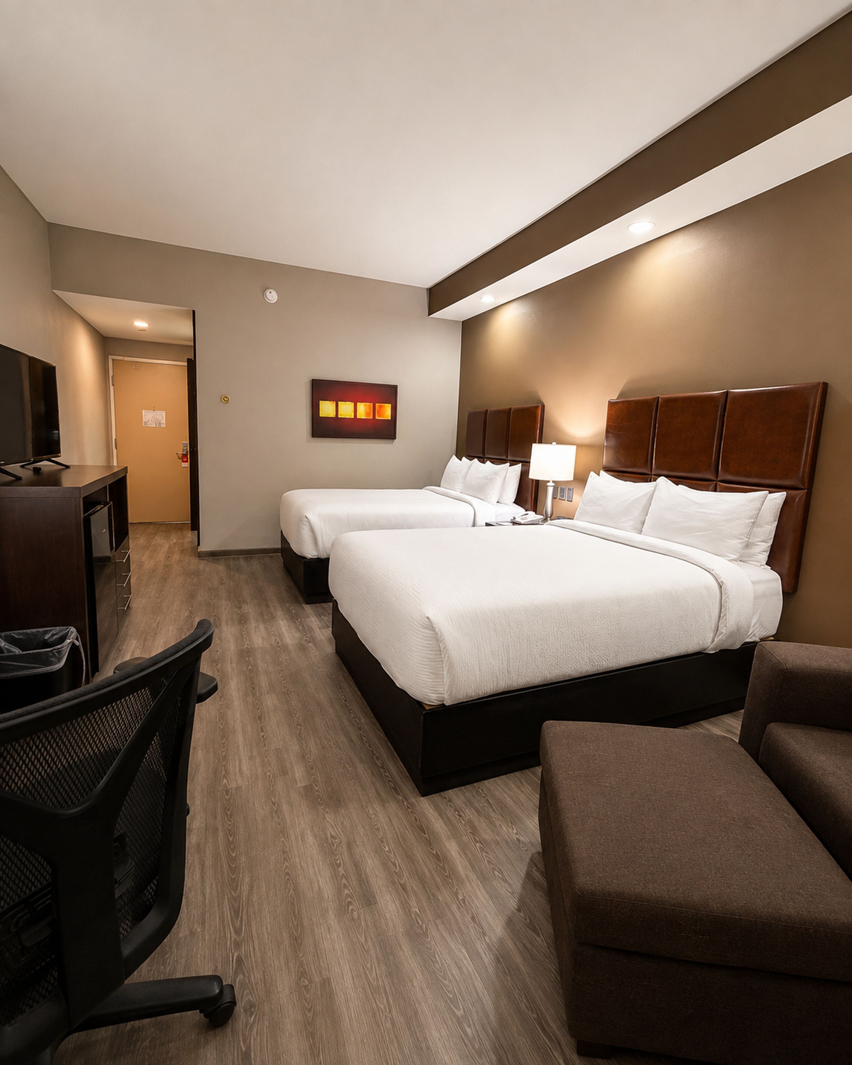 Habitación de hotel con dos camas, un escritorio, una silla y un televisor.