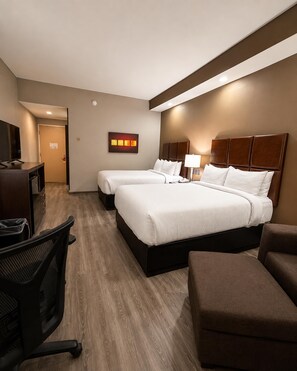 A hotel room with two beds, a desk, a chair, and a TV.
