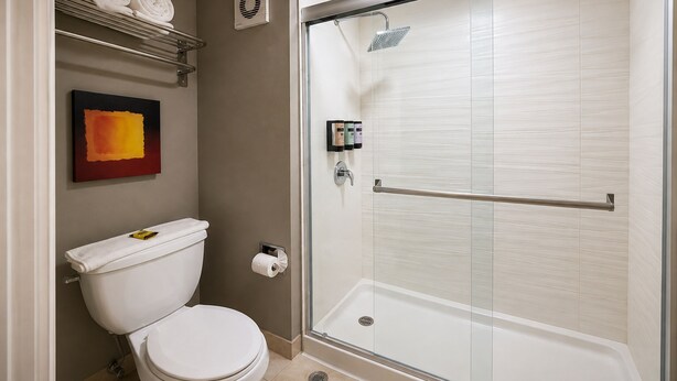 A modern bathroom with a toilet, a glass-enclosed shower, and a towel rack with folded towels. - Best Western Plus Monterrey Airport (Apodaca)