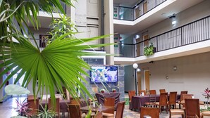 Un espacio interior de varios niveles con mesas y sillas para comer, una pantalla de televisión y plantas en macetas.