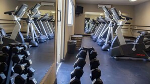 Un gimnasio con cintas de correr, mancuernas y un televisor en la pared.