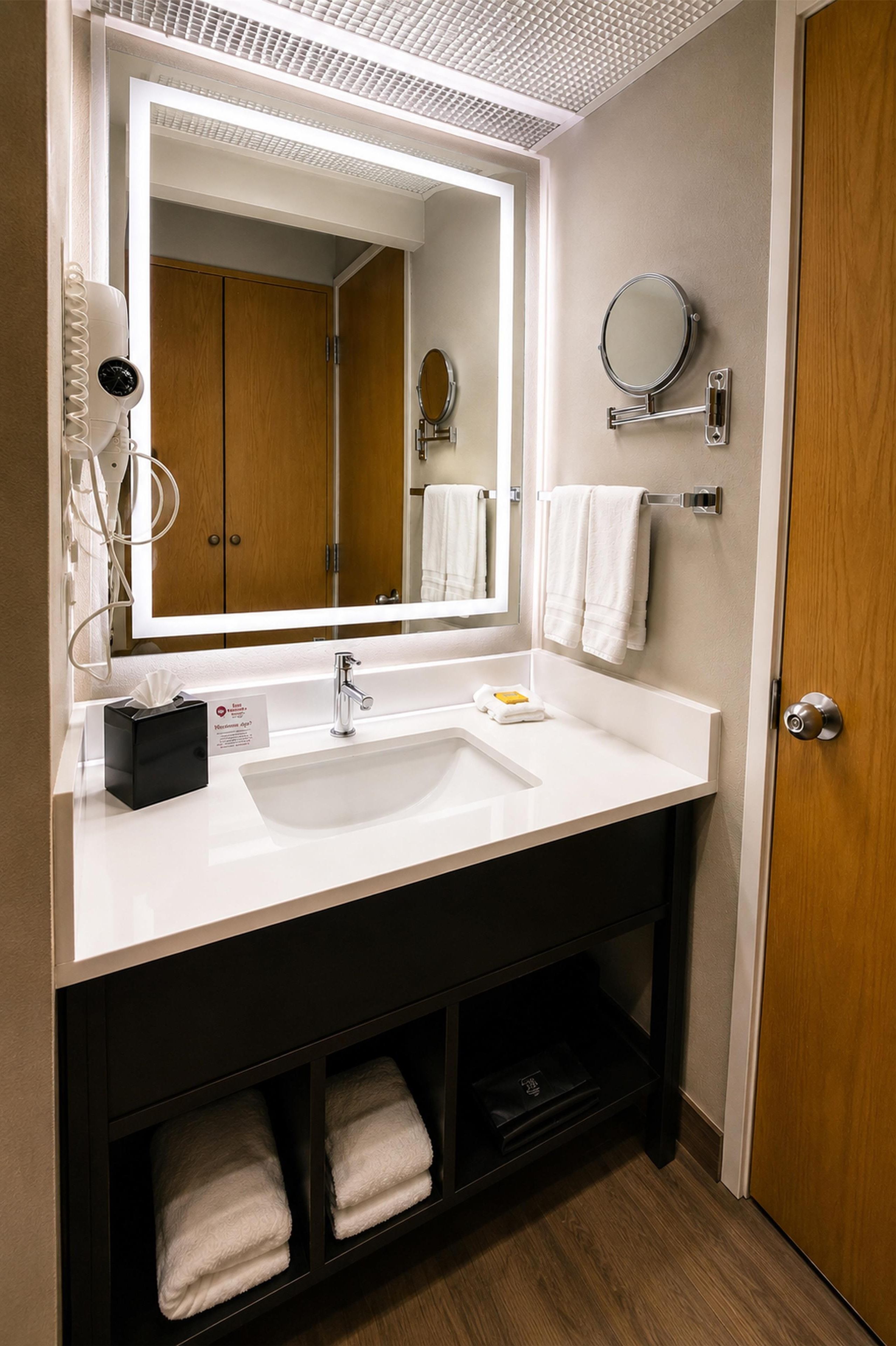 A modern bathroom with a white sink, a mirror, a towel rack, and a wooden door.