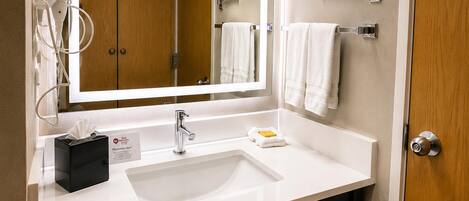 A modern bathroom with a white sink, a mirror, a towel rack, and a wooden door.