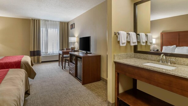 Une chambre d’hôtel avec deux lits, un bureau avec une télévision, une lampe de bureau, une coiffeuse avec un lavabo et un grand miroir.