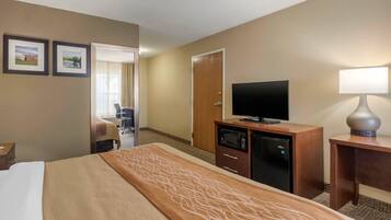 Habitación de hotel con cama, escritorio con televisor, microondas y lámpara. Se ve una puerta que da a otra habitación y una silla en un rincón.