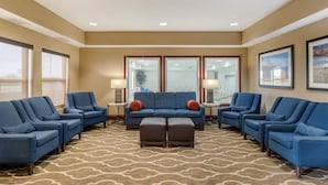 Un hall d’hôtel avec un tapis à motifs, des fauteuils bleus, un canapé et une table basse.