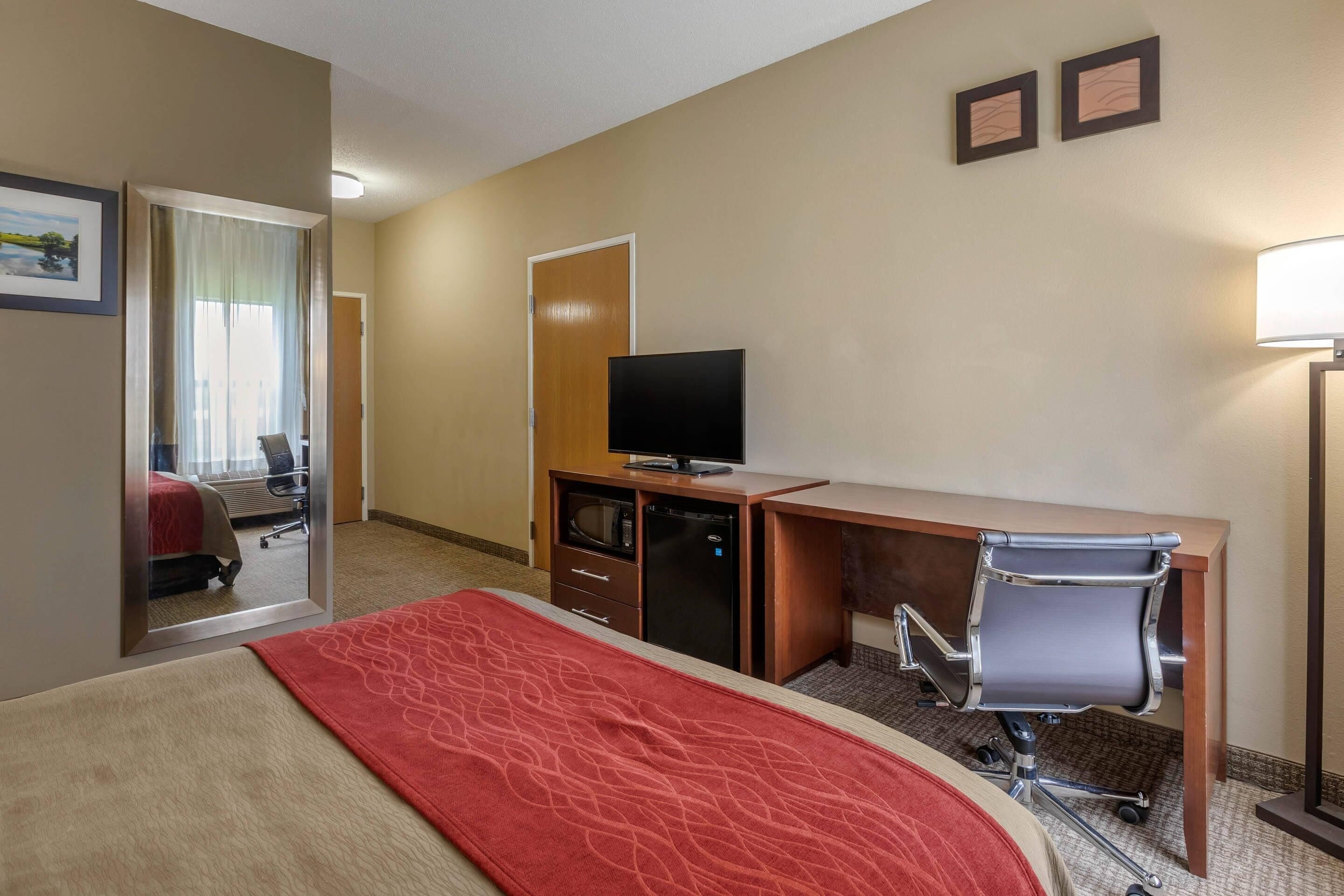 A hotel room with a bed, a desk with a computer, a television, a chair, and a lamp.