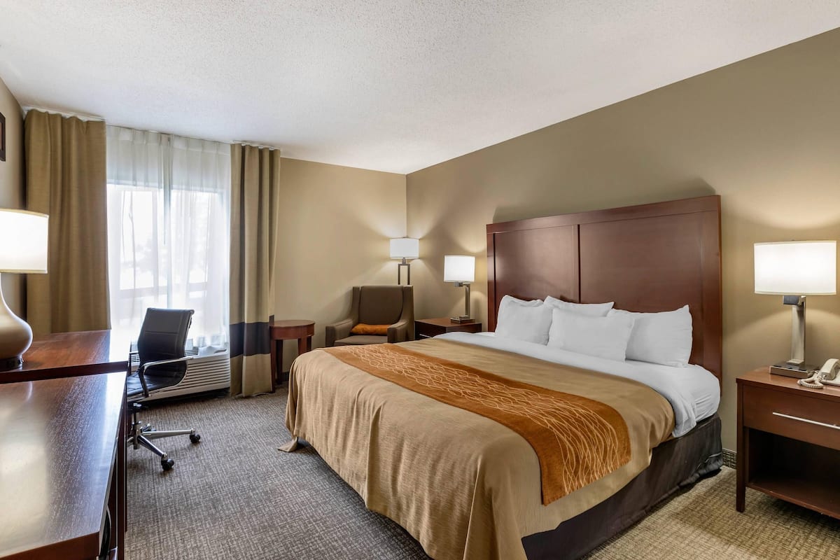 Una habitación de hotel con una cama grande, un escritorio, una silla y una lámpara.