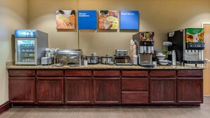 Un buffet de petit-déjeuner d’hôtel comprenant un réfrigérateur, une machine à café et un distributeur de jus.