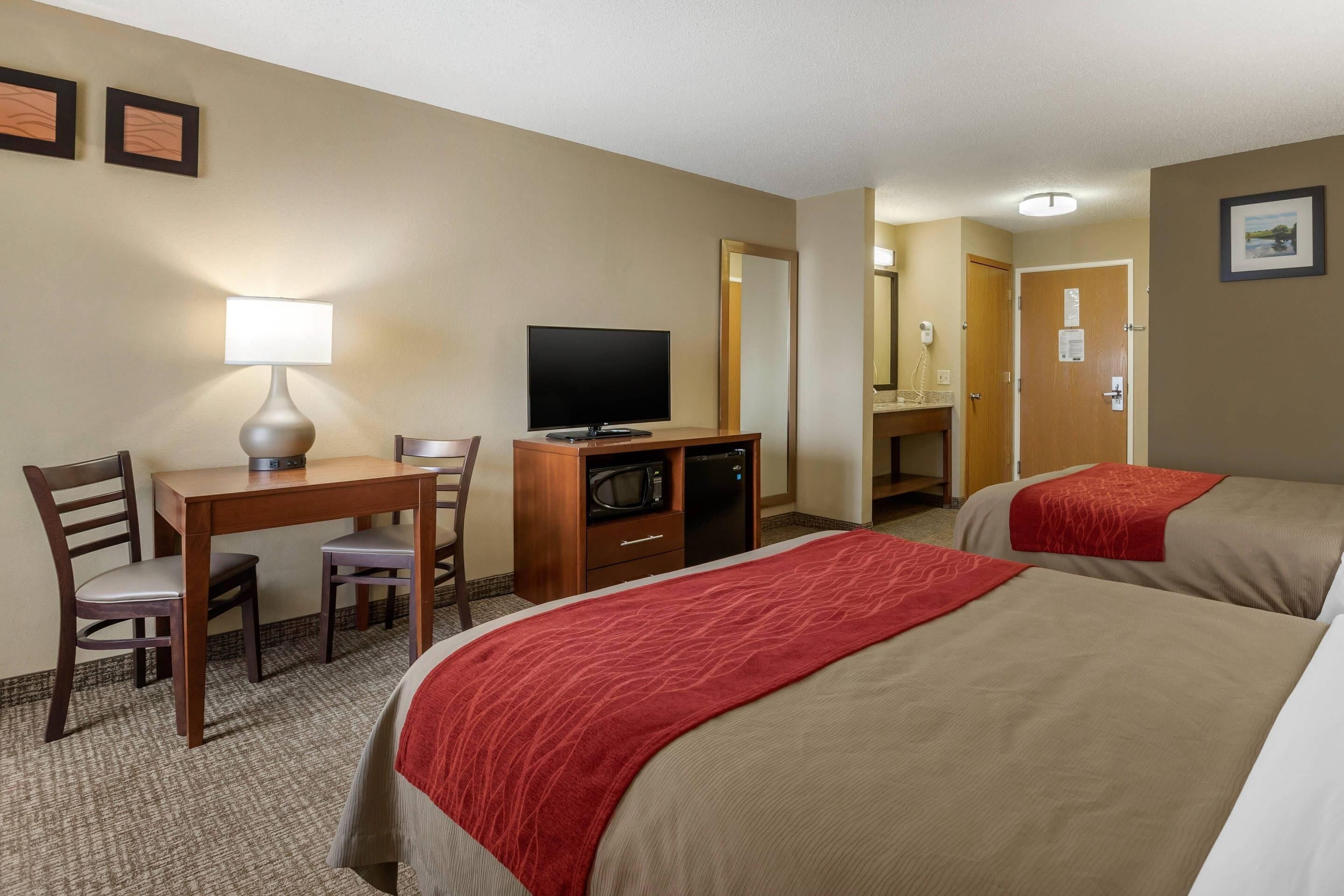 A hotel room with two beds, a desk with a television, a microwave, and a lamp.