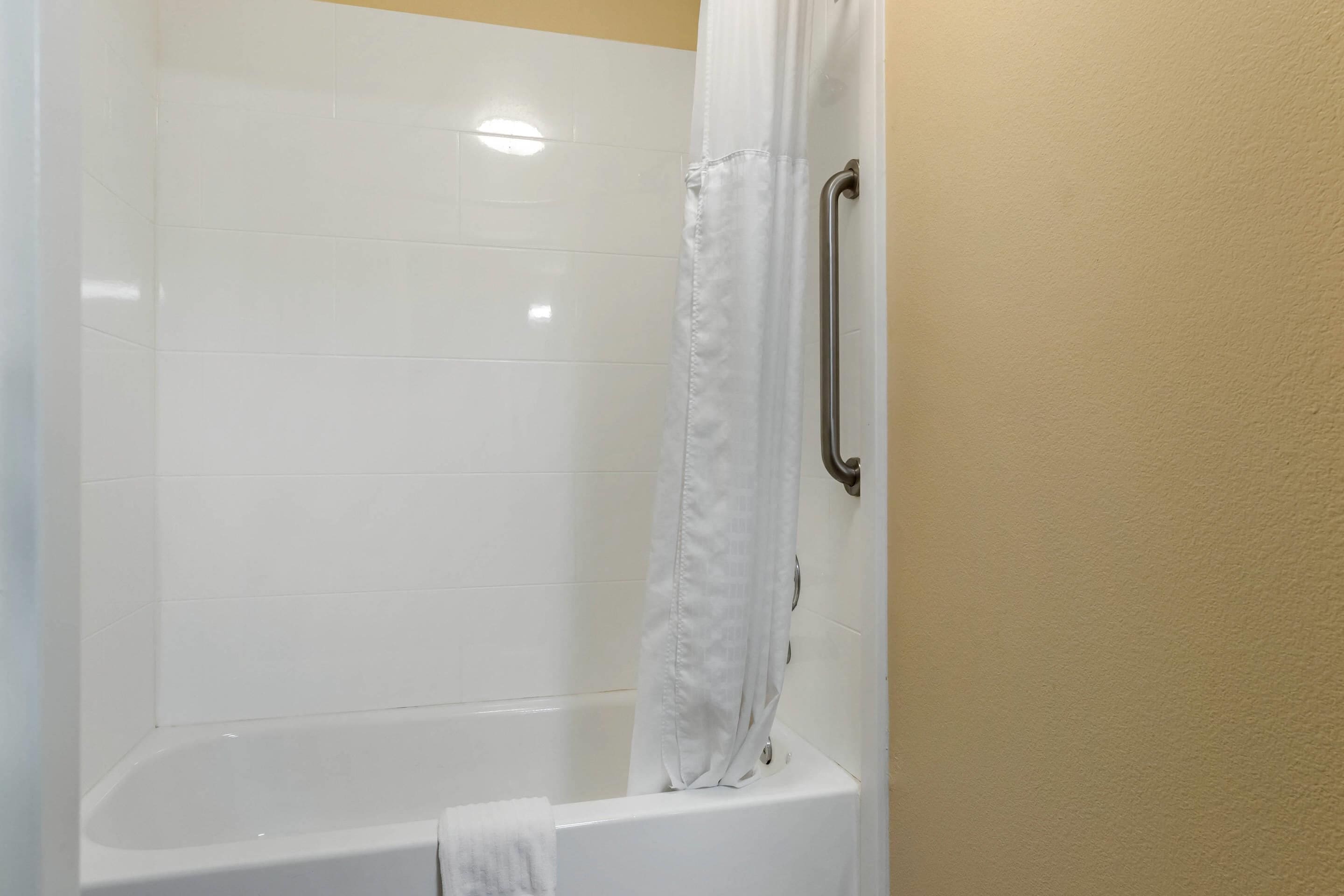 A white bathtub with a shower curtain and a grab bar.