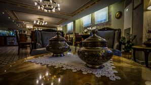 A table with two ornate metal containers on a lace doily in a warmly lit room with a patterned floor, a bar in the background, and a view of the outside through a window. - Yusufpasa Konagi - Special Class (Istanbul)