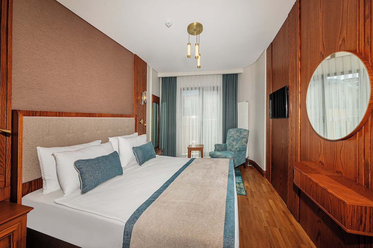 A hotel room with a large bed, a wooden headboard, a round mirror, a television, and a small table.