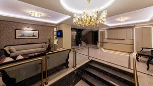Un vestíbul d'hotel modern amb una escala, una làmpada de cristall, un sofà i una televisió.