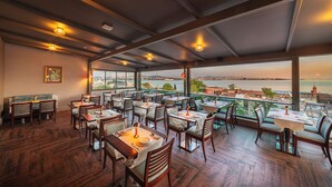Restaurant amb sòl de fusta i taules preparades per dinar, amb vista a un paisatge idíl·lic d'aigua i edificis.