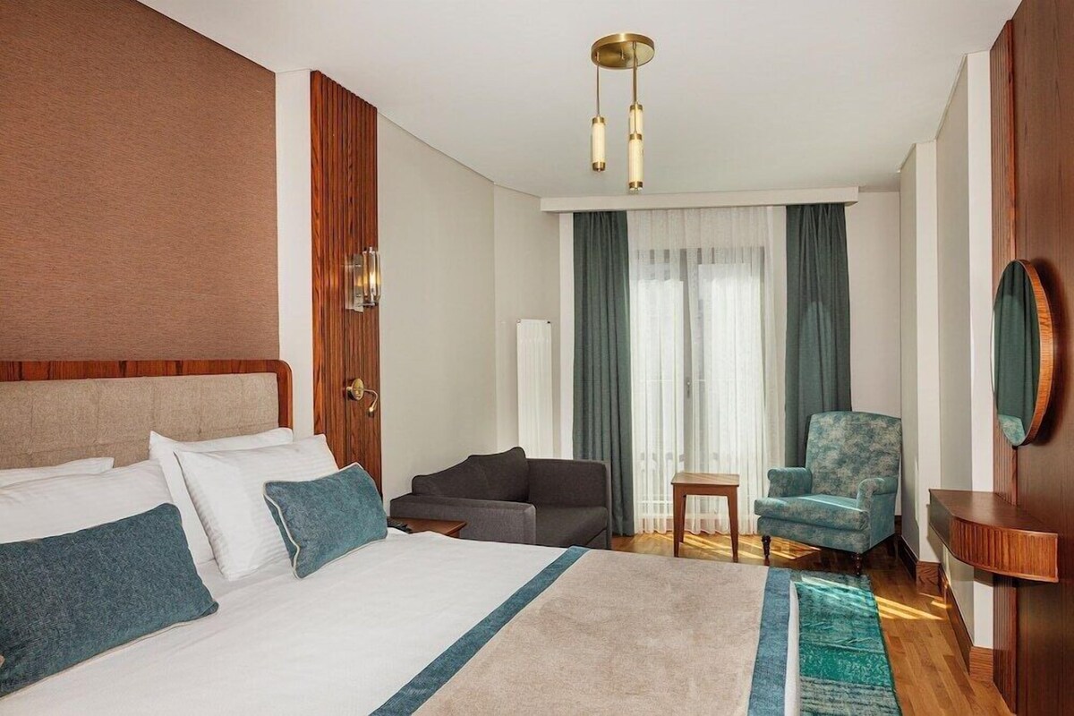 Une chambre d’hôtel avec un lit, un canapé, une chaise, une petite table et un miroir.
