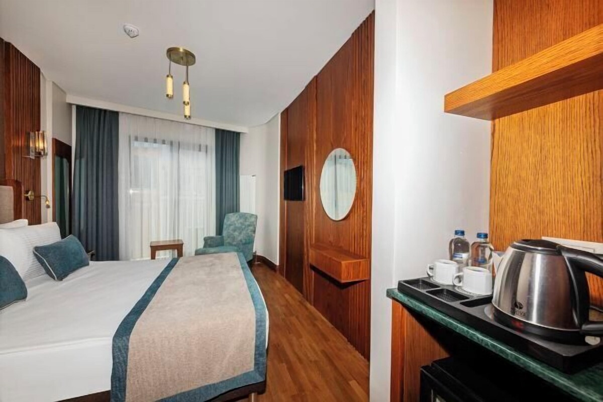 Une chambre d’hôtel avec un lit, un bureau doté d’une bouilloire, une chaise et un miroir rond accroché au mur.
