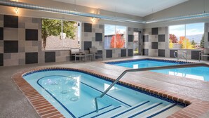 Un área de piscina interior moderna con vistas despejadas al exterior, un espacio de descanso y una piscina con borde de azulejos azules y marrones.