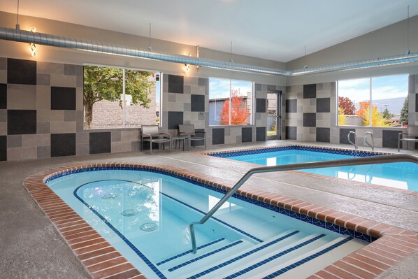 A modern indoor pool area with a clear view of the outside, a seating area, and a pool with a blue and brown tiled edge.