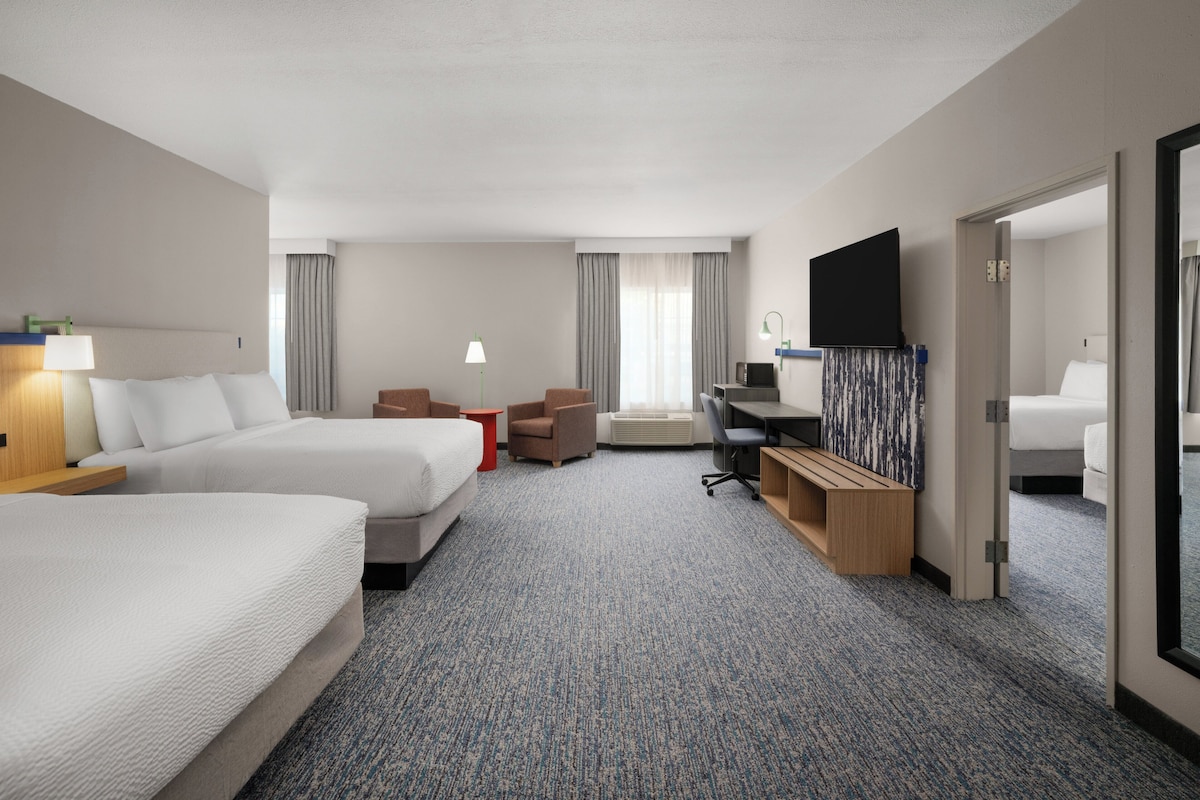 Habitación de hotel con dos camas, un escritorio, una silla, un televisor y una ventana con cortinas.