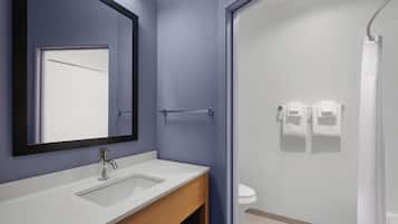 Un baño con lavamanos blanco, espejo, toallero y zona de ducha.
