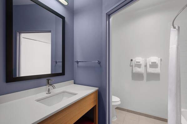 Un baño con lavamanos blanco, espejo, toallero y zona de ducha.