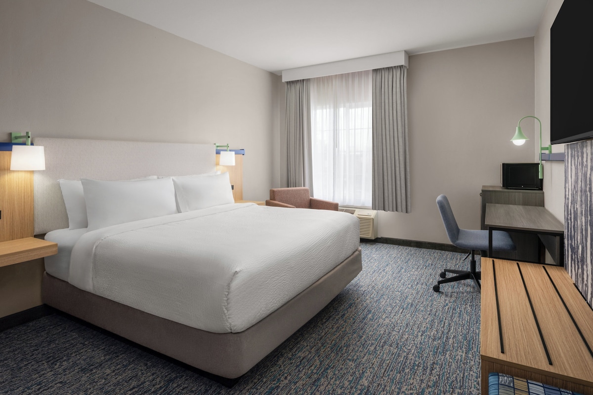 Habitación de hotel con una cama grande, un escritorio, una silla, un televisor y una ventana con cortinas.