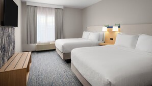 Habitación de hotel con dos camas, un televisor de pantalla plana, un banco de madera y una ventana con cortinas.