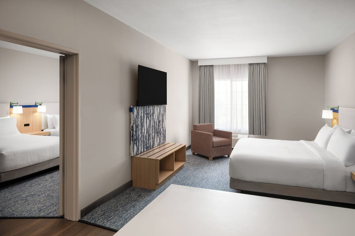 Habitación de hotel con cama, escritorio, silla, televisor y ventana con cortinas.