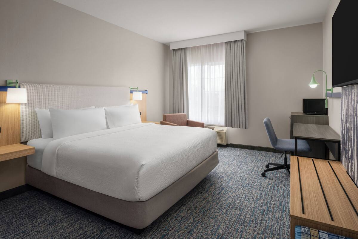 Habitación de hotel con una cama grande, un escritorio, una silla, un televisor y una ventana con cortinas.