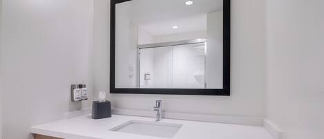 Een moderne badkamer met een witte wastafel, een spiegel met zwart frame en een houten opbergmeubel.
