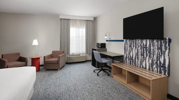 A hotel room with a bed, two armchairs, a desk with a computer, a TV, and a large abstract painting on the wall.