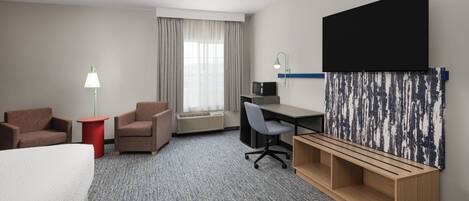Ett hotellrum med en säng, två fåtöljer, ett skrivbord med en dator, en tv och en stor, abstrakt målning på väggen.