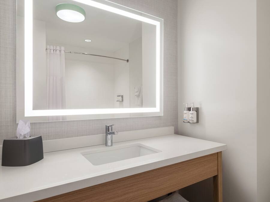 Un baño moderno con un espejo grande, un lavamanos blanco y una cortina de ducha.