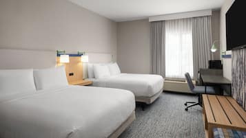 A hotel room with two beds, a desk, a chair, a television, and a window with curtains.