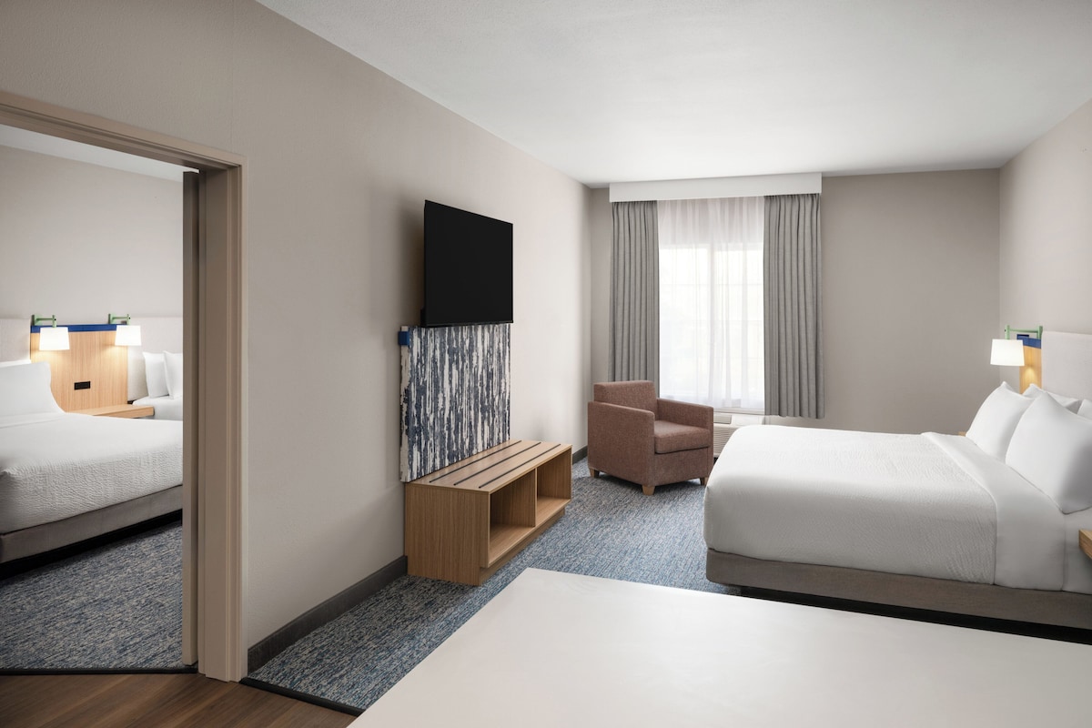Habitación de hotel con cama, escritorio, silla, televisor y ventana con cortinas.