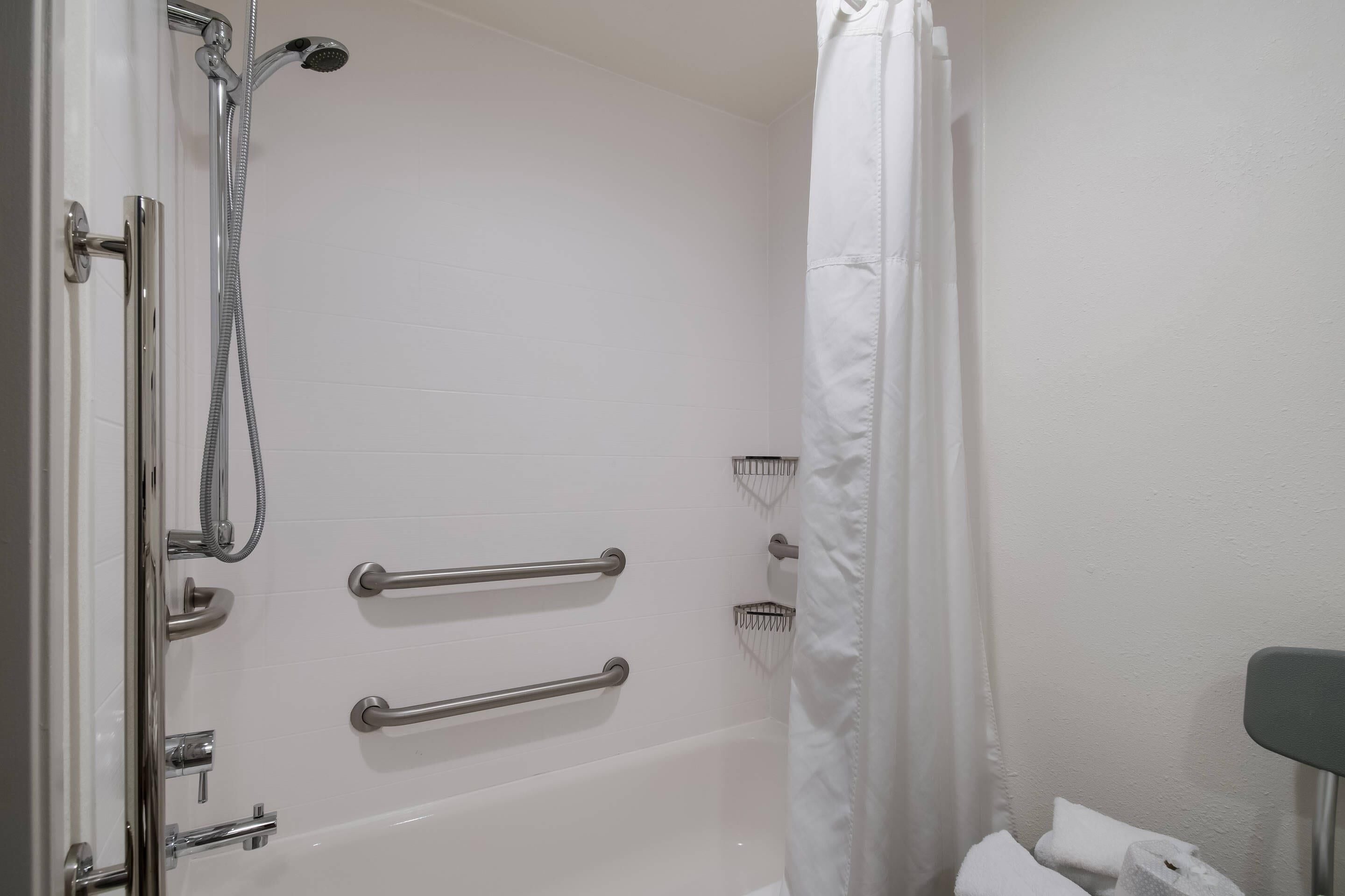 A bathroom with a bathtub, shower, and handrails.