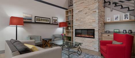 Una sala de estar moderna con chimenea, una mesa de centro de vidrio, un sillón rojo y una estantería.