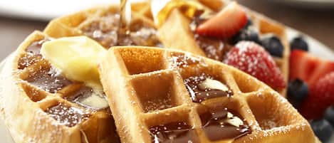 A plate of waffles with syrup, butter, and fruit.