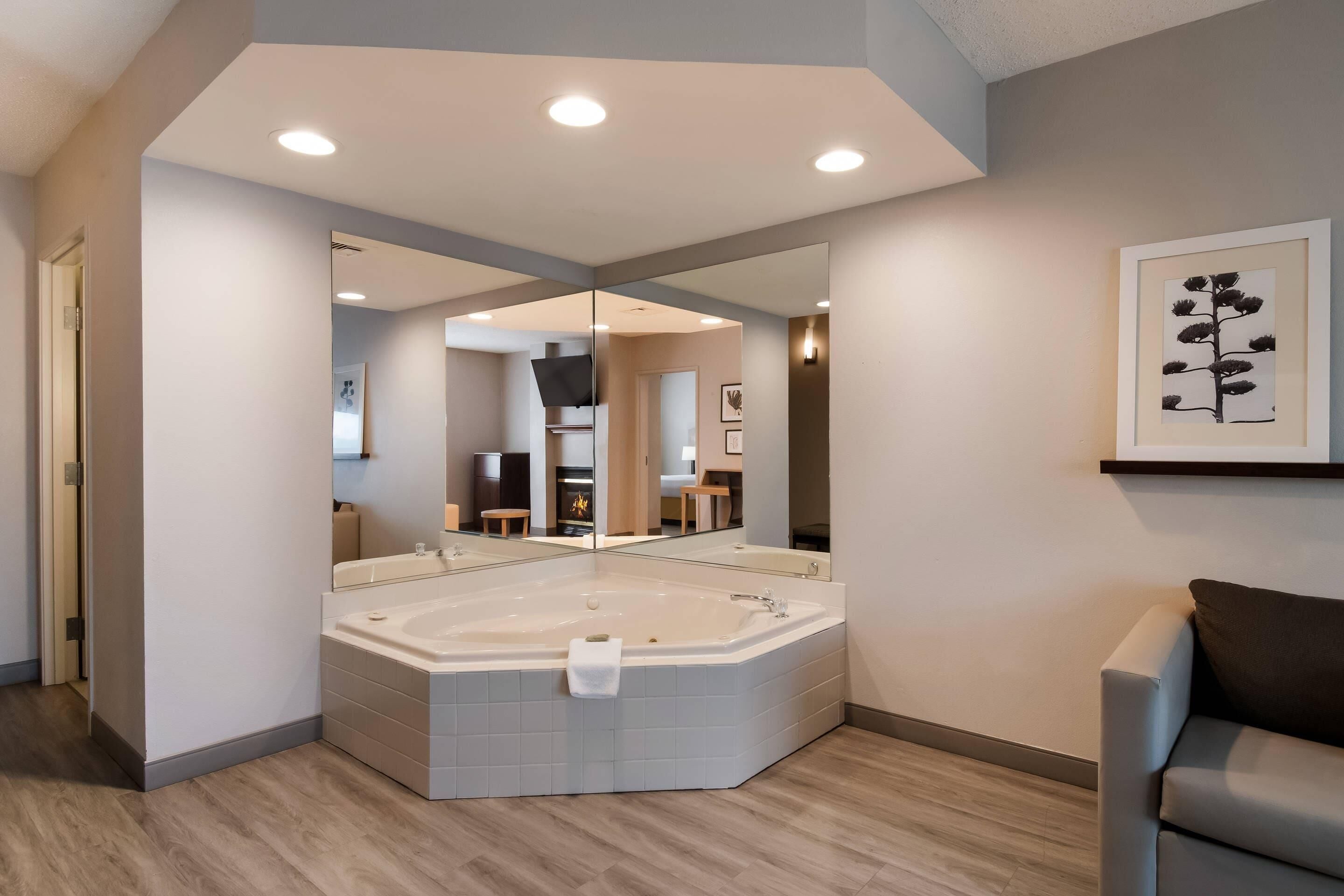 A modern bathroom with a large bathtub, a mirror, and a framed artwork on the wall.