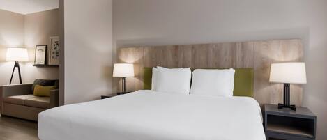 A hotel room with a large bed, two bedside tables with lamps, a sofa, and a wall-mounted headboard.