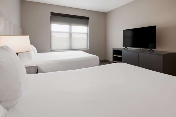Two single beds with white linens, flat-screen TV, and a large window with a white blind.