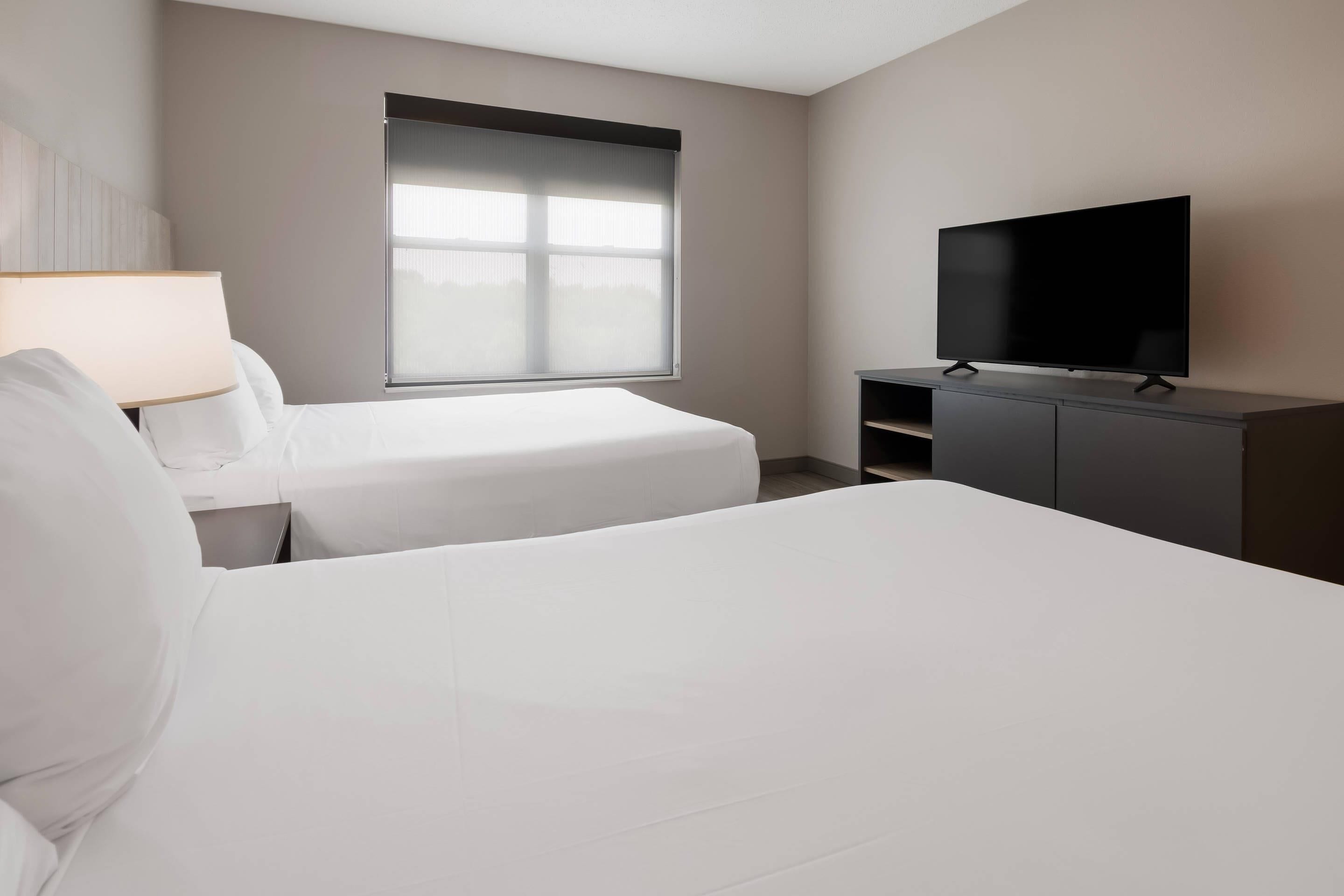 A hotel room with two beds, a TV on a cabinet, and a window with blinds.