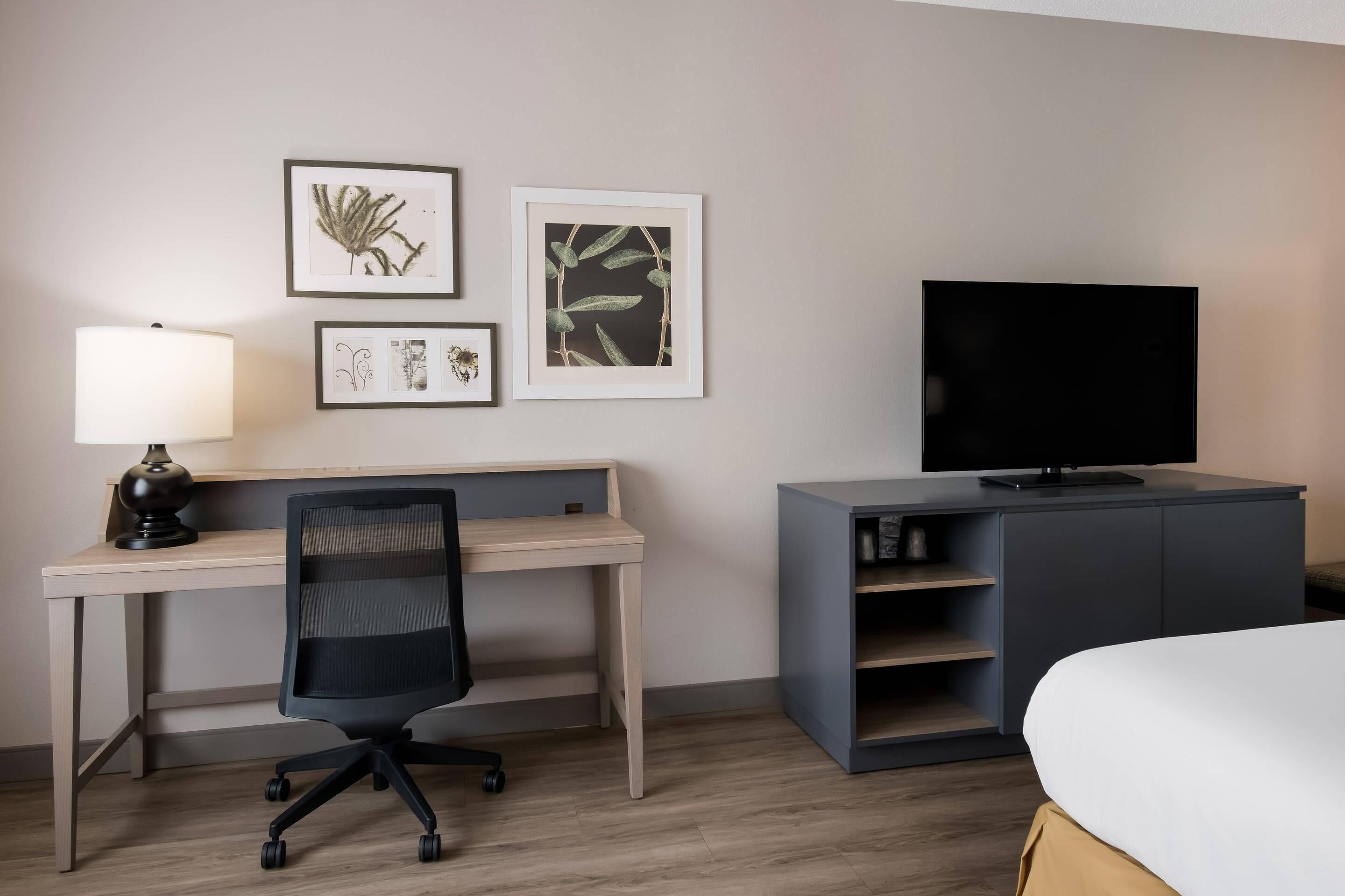 A hotel room with a desk, chair, TV, and bed.