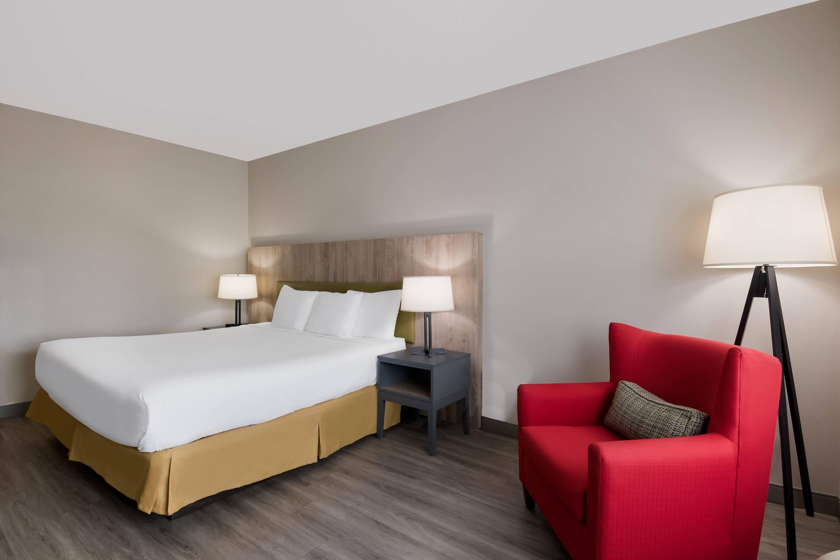 A hotel room with a bed, two bedside tables, a red armchair, and a floor lamp.