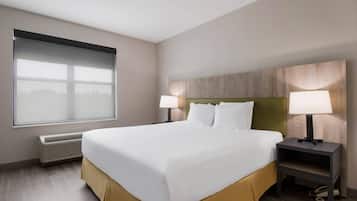 Habitación de hotel con una cama grande, dos mesitas de noche con lámparas, una ventana con persianas y un calentador fijado a la pared.