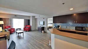 Una habitación de hotel moderna con sala de estar, sillones rojos, un televisor de pantalla plana, una cocina con microondas y un ventanal grande.