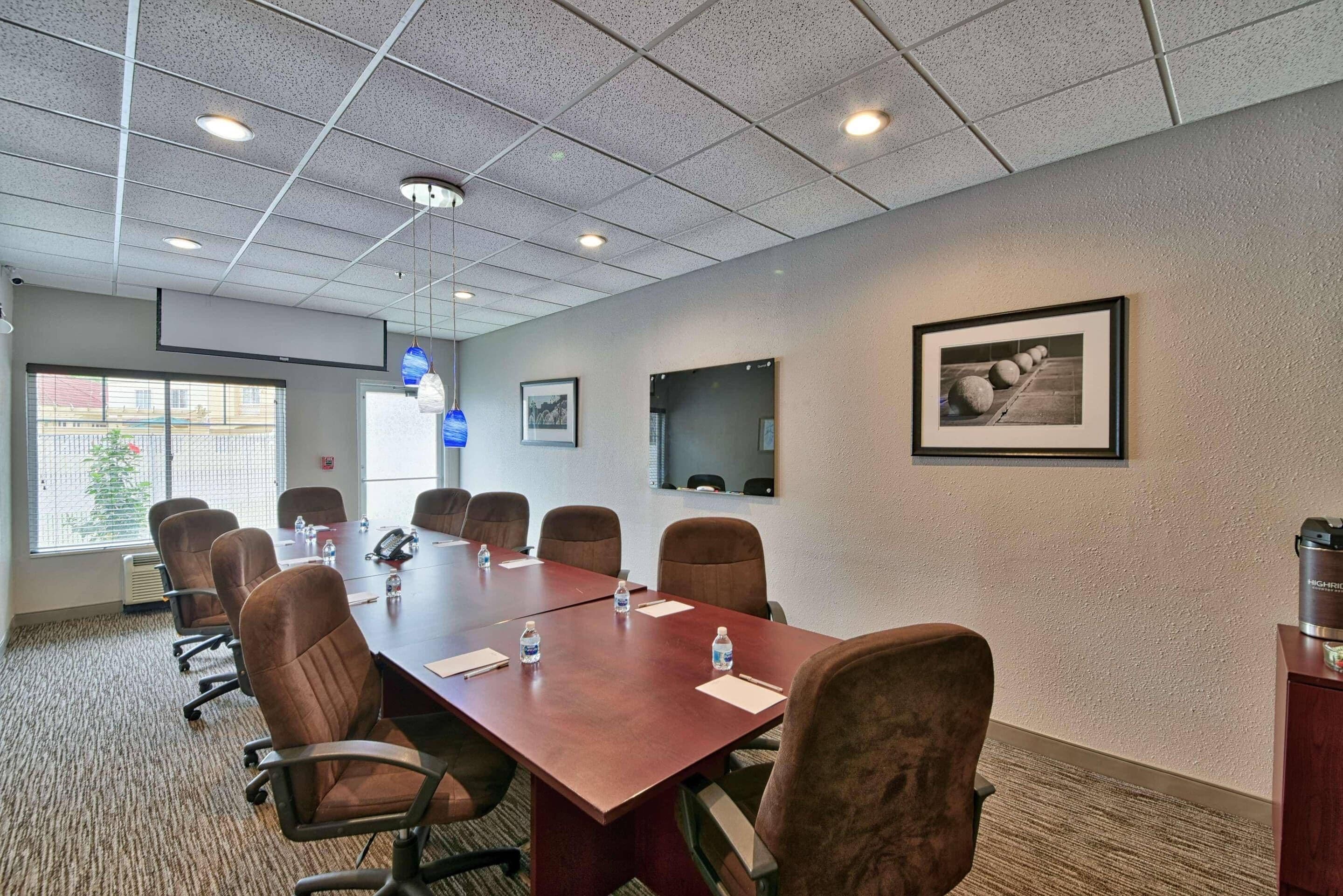 A conference room with a long table, brown chairs, water bottles, and framed pictures on the walls.