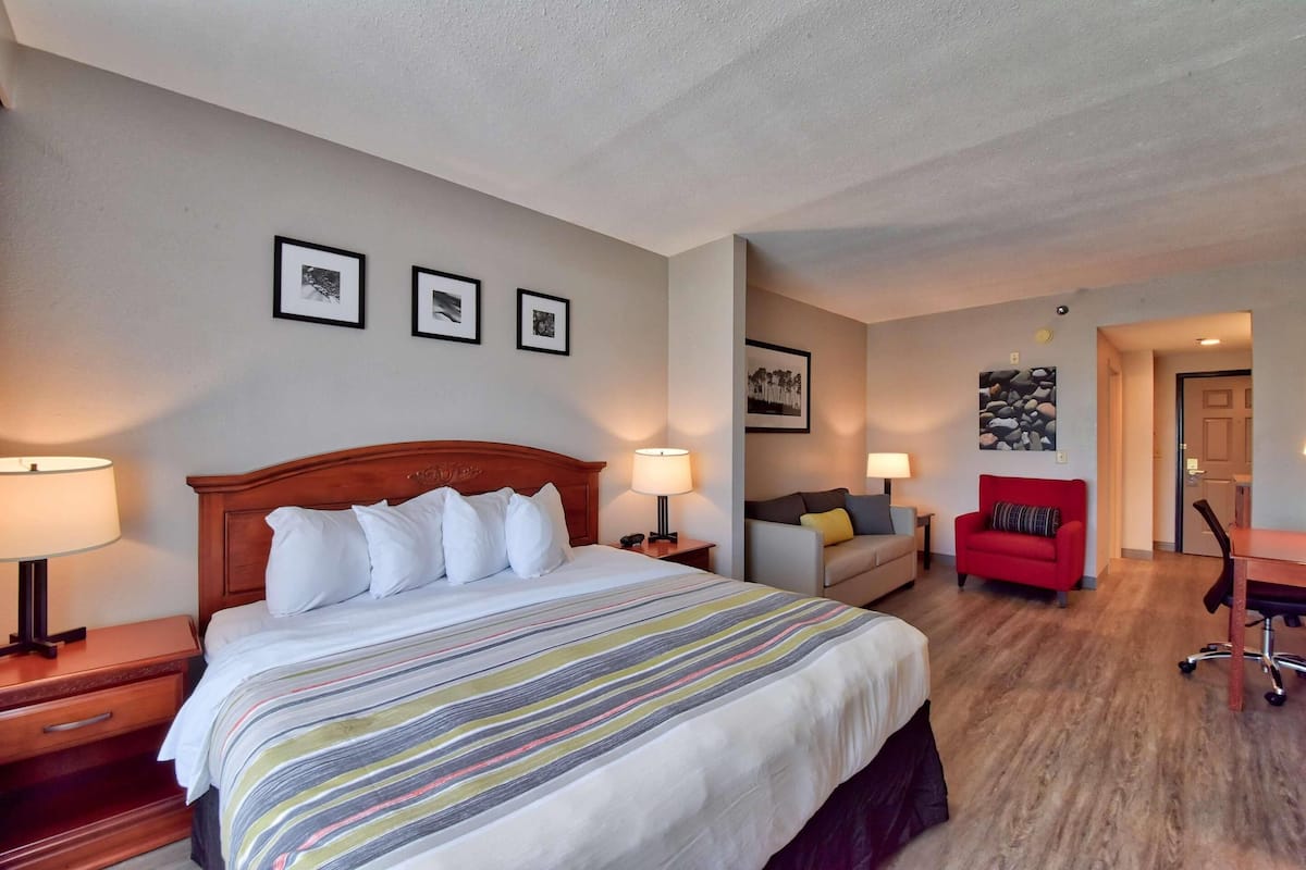 A hotel room with a bed, a desk, a chair, and a sofa. There are framed pictures on the wall.