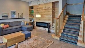Una sala de estar moderna con un sofá seccional gris, estanterías de madera, una chimenea y una escalera con alfombra estampada.